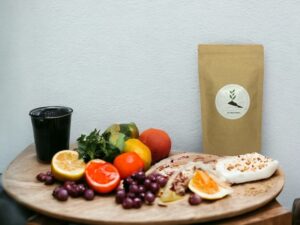 Bild eines AY Natural Doypacks auf einem Tisch umgeben von verschiedenen Früchten mit einer weißen Wand im Hintergrund