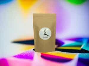 Brauner Doypack von AY Natural vor regenbogenfarbenem Hintergrund