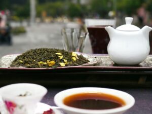 Hier liegt unser AY Natural Grüntee aus Japan auf einem Tisch serviert mit einer weißen Teekanne und einer Tee Tasse Dieser Tee verspricht einen unvergleichlichen Genuss und lädt dazu ein die reiche Tradition des japanischen Grüntees zu erleben Gönn dir eine Auszeit und genieße den einzigartigen Geschmack dieses besonderen Tees