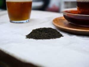 Auf dem Tisch liegt der lose AY Natural Tee Eine Tasse ist mit Tee gefüllt erkennbar an seiner dunklen Farbe Es ist der schwarze Darjeeling First Flush Tee