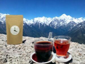 Auf einem Stein liegt der AY Natural Doypack Davor stehen Tassen mit Tee Im Hintergrund sind majestätische Gebirge zu sehen Es handelt sich um den Schwarztee aus dem Himalaya