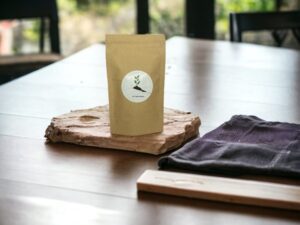 Hier präsentiert sich unser AY Natural Tee aus Südindien in einem eleganten Doypack auf einem Tisch Die entspannte Atmosphäre wird durch das daneben liegende Handtuch betont Genieße die Eleganz und den einzigartigen Geschmack dieses südindischen Tees