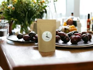 Dieses Bild zeigt unseren AY Natural Doypack gefüllt mit den verlockenden Teemischungen Olivenparadies auf einem Tisch Die reichhaltige Präsenz von Oliven neben dem Doypack unterstreicht die Exklusivität und Qualität dieser Teesorte Olivenparadies bietet eine harmonische Fusion von Oliven und Teekräutern die für ein einzigartiges und erfrischendes Geschmackserlebnis sorgt